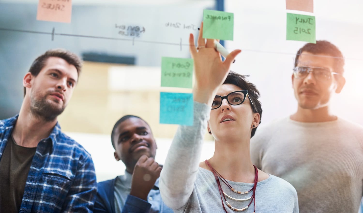 Team collaborating and brainstorming with sticky notes on a glass board in a bright office setting.