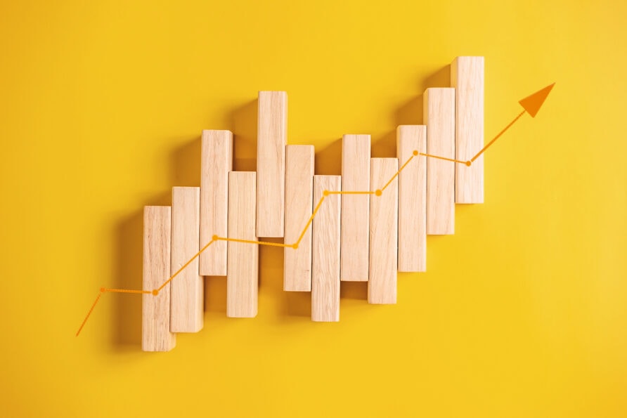 Wooden blocks arranged in a staggered upward pattern with an orange arrow indicating growth on a yellow background.