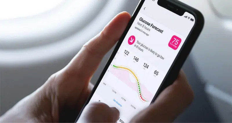 Person holding a smartphone displaying a glucose forecast app with a graph and measurements.