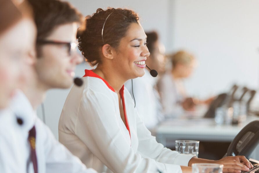 Customer service representatives wearing headsets, seated at desks, and assisting customers in a bright office.