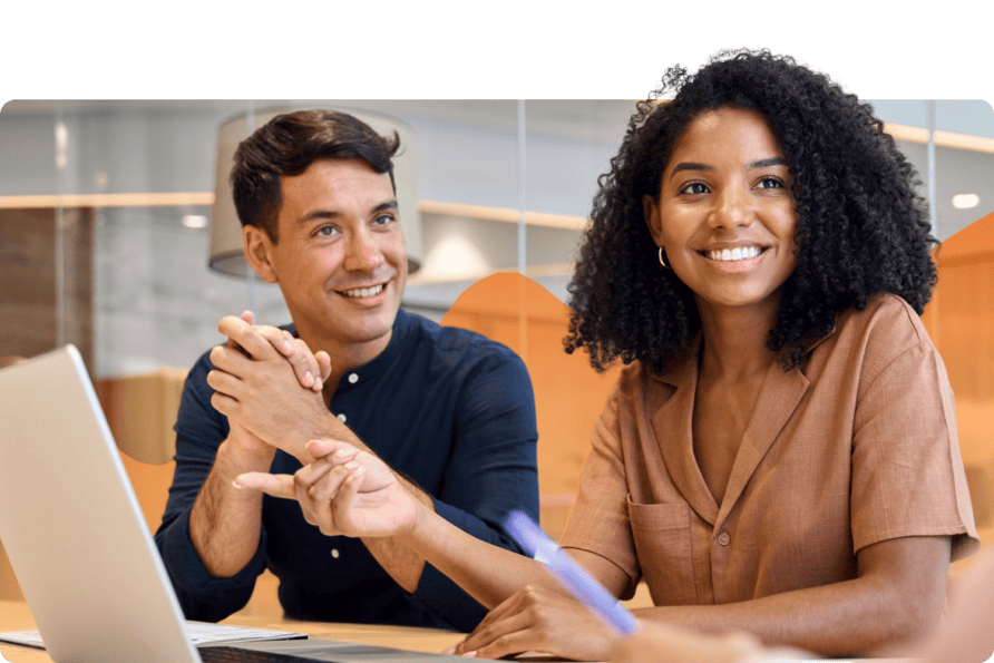 Two colleagues smiling while working together on a laptop in a bright office.